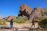 An older woman in a blue skirt, walking in front of a large rock in a national park