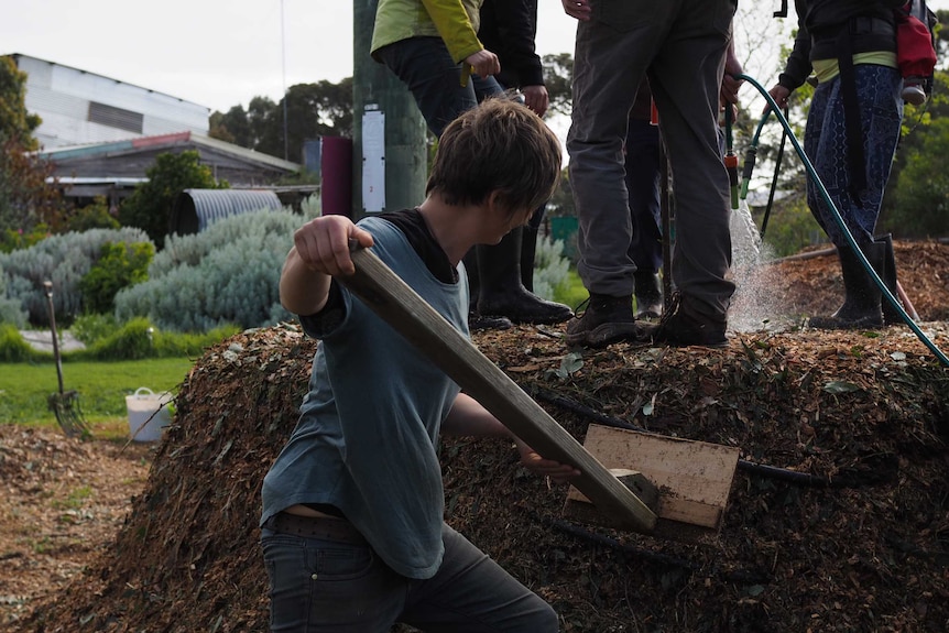 Compacting the oxygen out of the compost heap by hand with a large wooden paddle