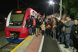 A crowd with a ribbon in the dark next to a train at a station