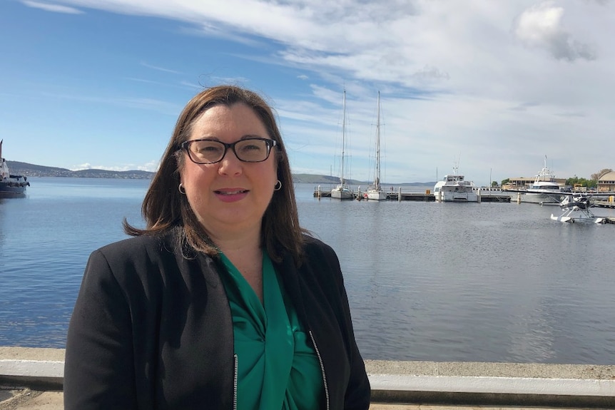 A woman wearing glasses stands on a waterfront dock