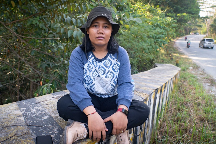 A young woman sits cross legged on a bridge near a road