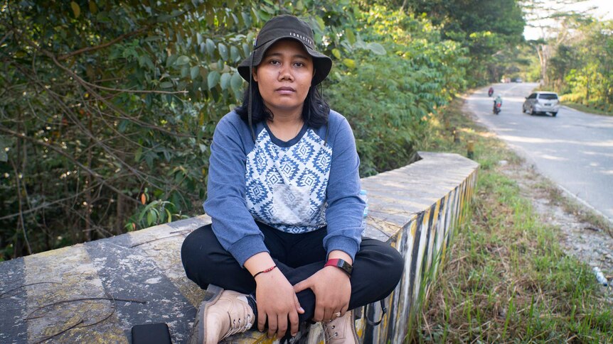 A young woman sits cross legged on a bridge near a road