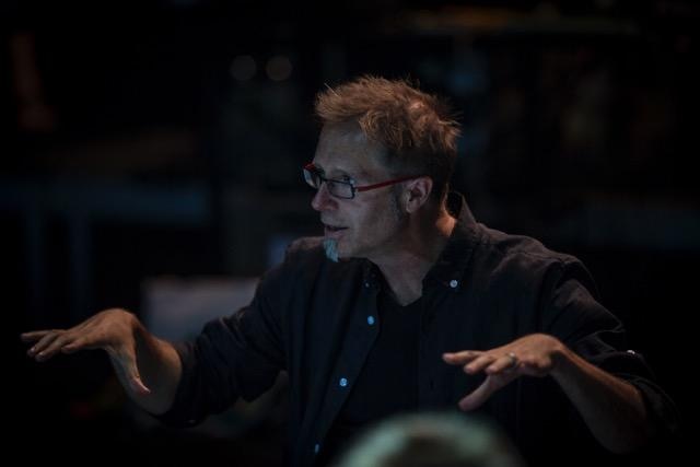 Professor Doser with glasses and spikey hair animatedly speaking in a dark room
