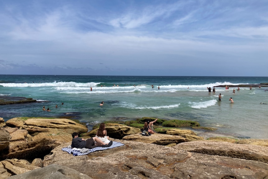 A couple of people rest on the rocks at Mackenzies Bay in Sydney