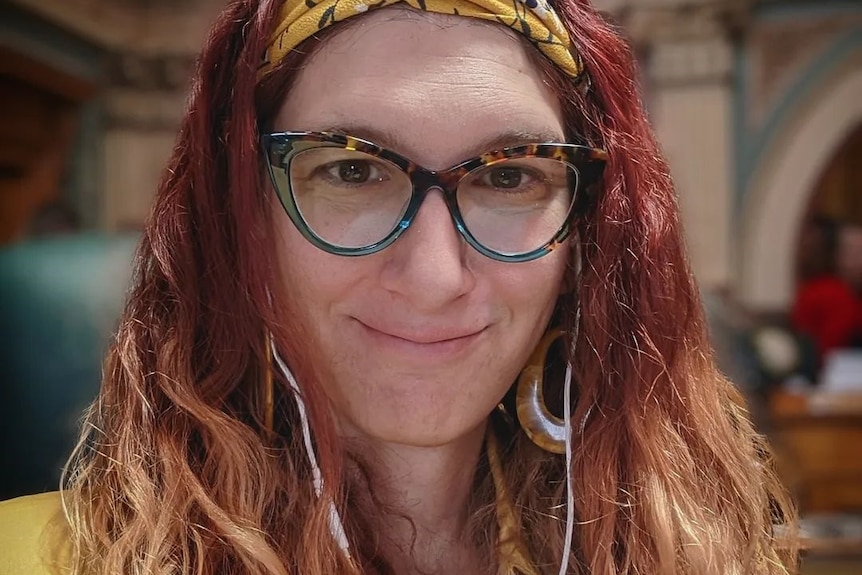 Une femme aux cheveux roux ondulés et aux lunettes à monture épaisse