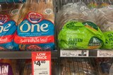 Two loaves of bread on a supermarket shelf, one with blue and red label and one with a green label that says gluten free