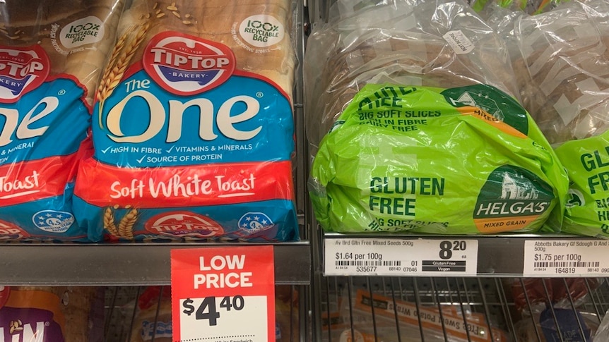 Two loaves of bread on a supermarket shelf, one with blue and red label and one with a green label that says gluten free