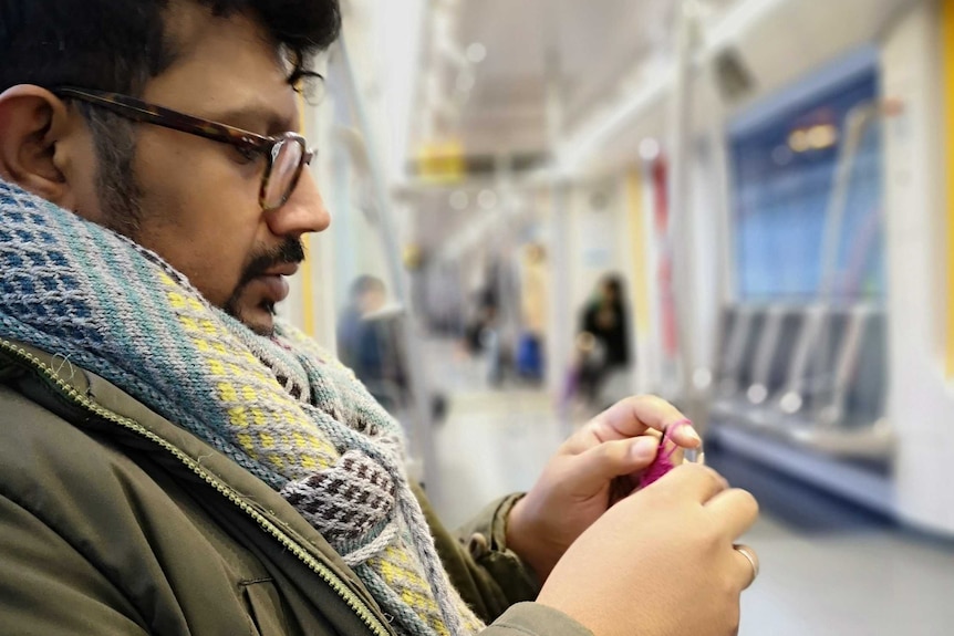 A man sits on a subway train and knits