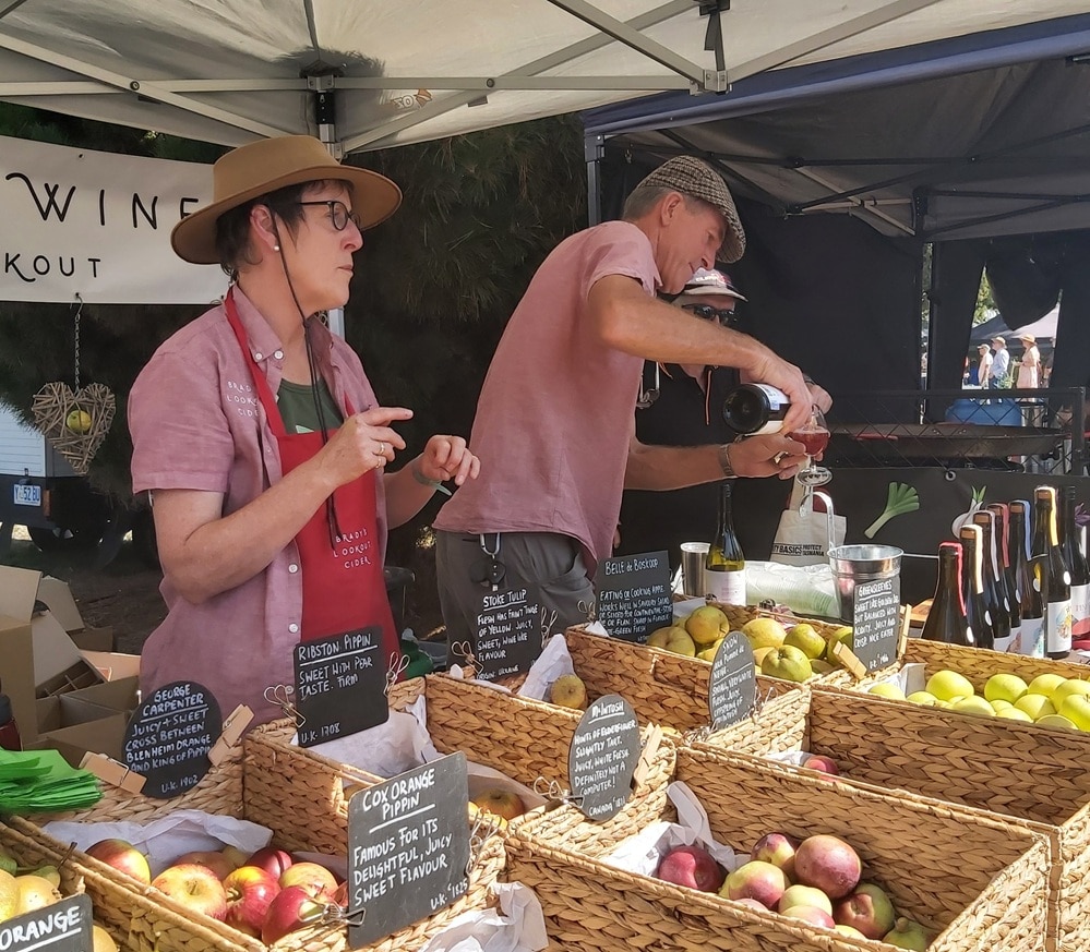 A man and a woman serving customers apple and cider at a farmers market