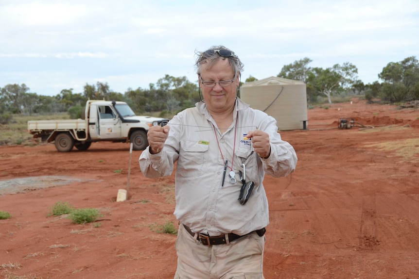 A man in the Australian desert holding divining rods.