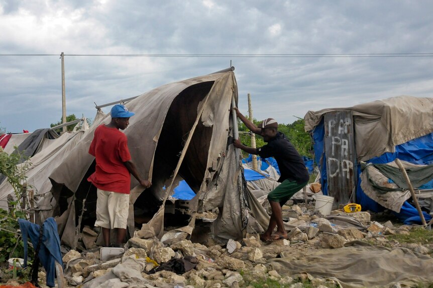 Haitians living in a camp built for people affected by the January 2010 earthquake try to repair their tent that was destroyed by Tropical Storm Isaac.