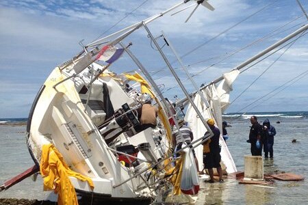 A yacht on its side on a reef being inspected by police. 