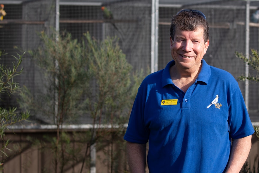 Man standing in front of bird enclosures.