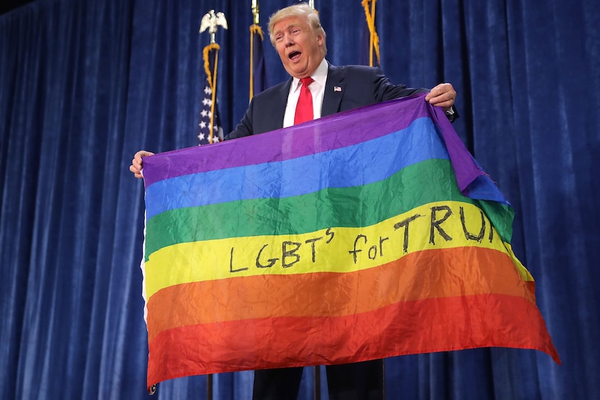 Donald Trump holding rainbow flag with words 'LGBTs for Trump' written on it. 