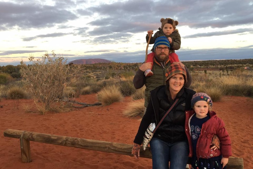 A man, woman and two small children standing near Yulara/Ayres Rock.