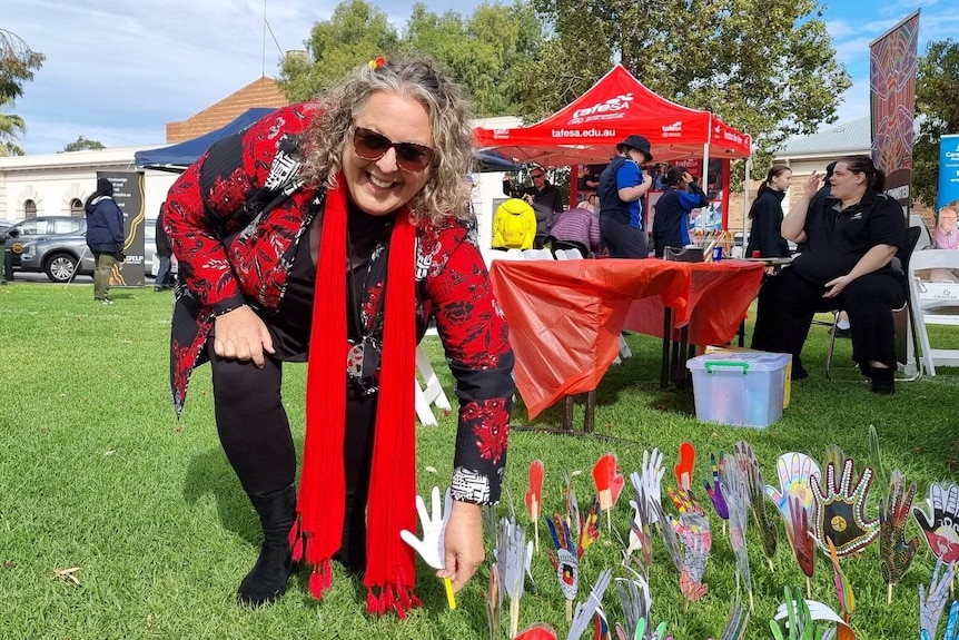 A woman bending down smiling - sticking a coloured hand drawing into the ground 