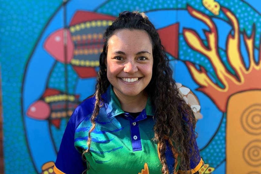 Kirby Barker smiling in front of Indigenous mural in story about reconciliation and early childhood.