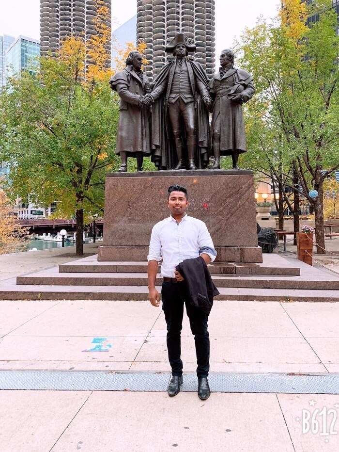 A man stands in front of a statue of three men in a park in Chicago.