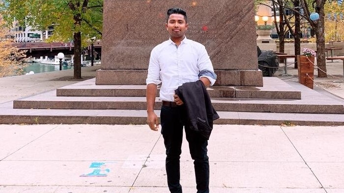 A man stands in front of a statue of three men in a park in Chicago.