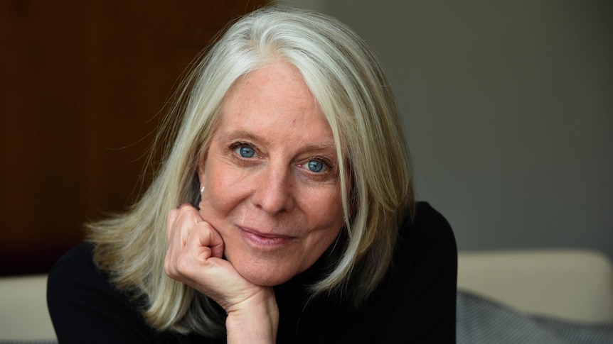 A white woman with grey hair and blue eyes looks into the camera.
