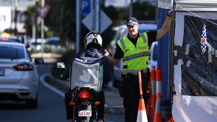 A police officer inspects a motorbike delivery rider at a road check point