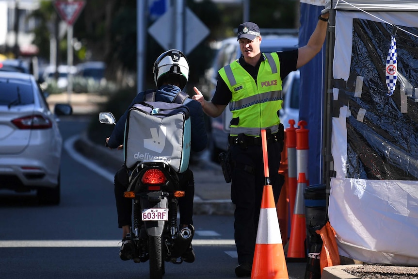 A police officer inspects a motorbike delivery rider at a road check point