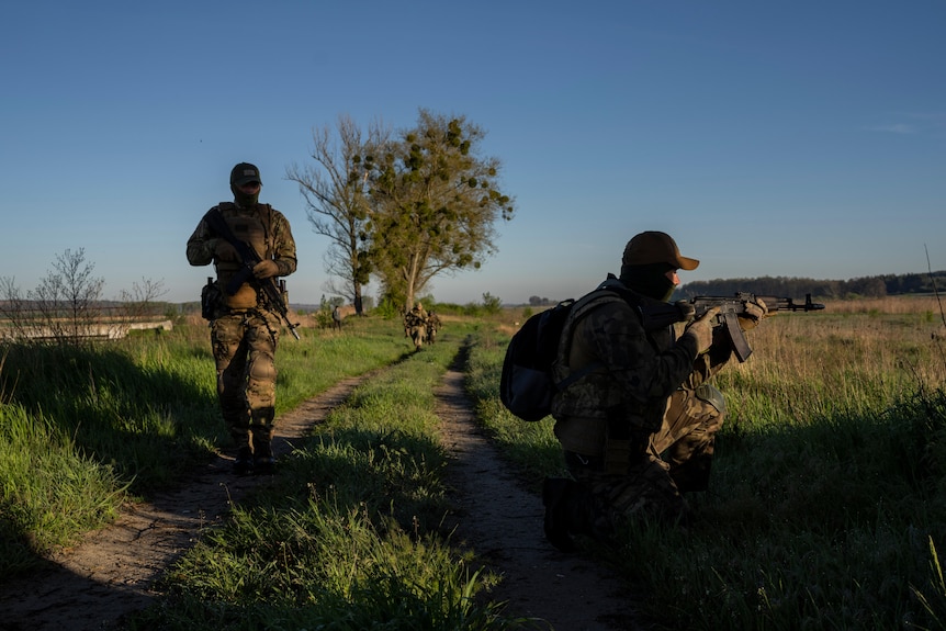 Ukrainian soldiers crouch in shadow near a field during military training