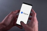 Hands hold a smartphone showing the Signal app logo