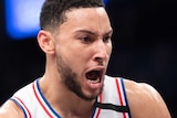 Ben Simmons holds the basketball and screams, wearing a white basketball singlet