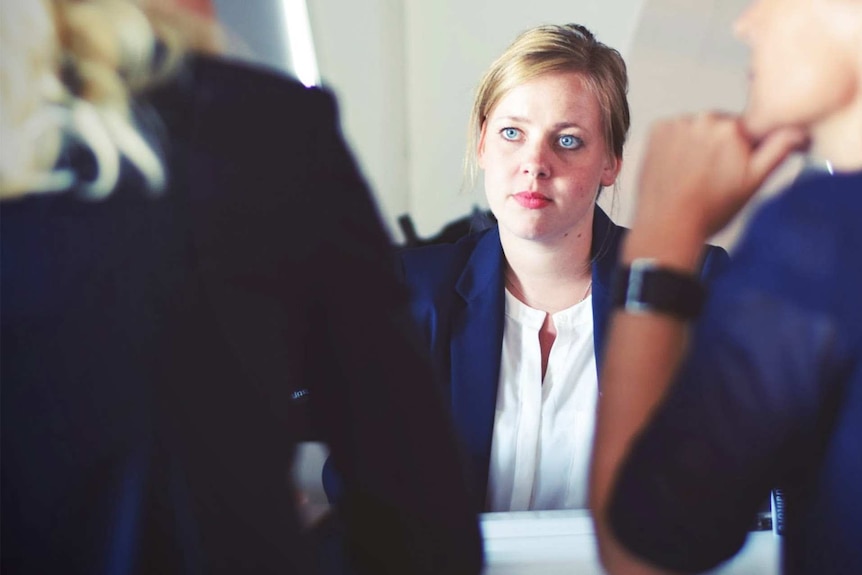Woman looking apprehensive in meeting at work to depict what to do when you face pregnancy discrimination.