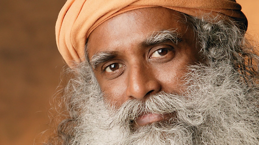 portrait of South Asian man with long wavy beard and moustache wearing an orange turban and light brown robes gazing forwards