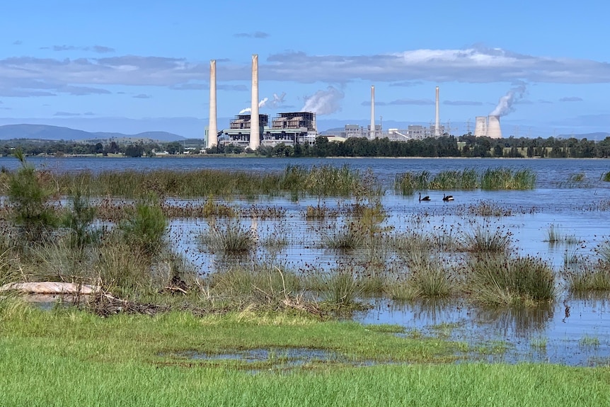 A calm blue lake with a large power station in the background.