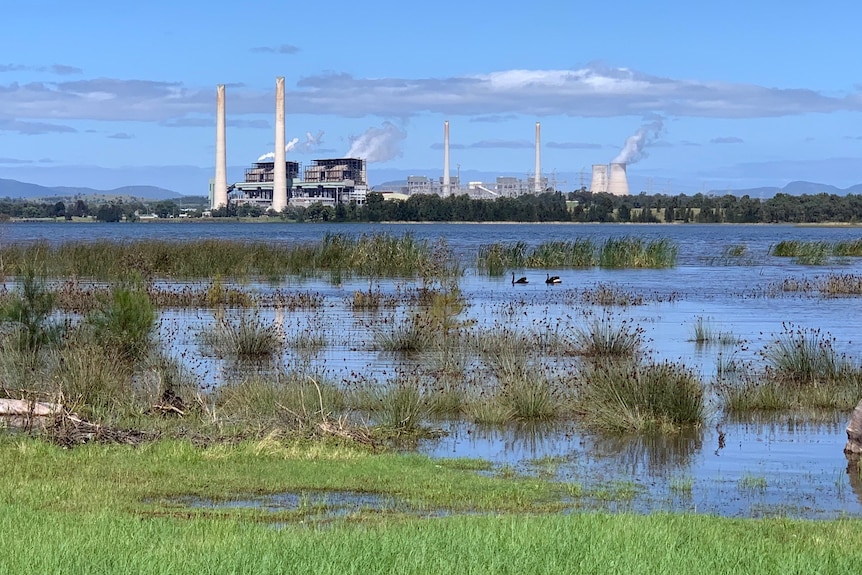 A calm blue lake with a large power station in the background.