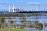 A calm blue lake with a large power station in the background.