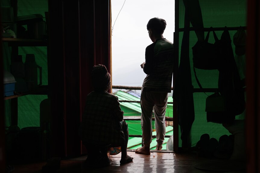 Two people in their home in Myanmar overlooking a camp