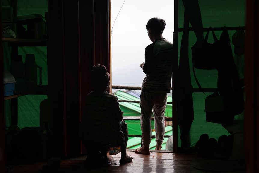 Two people in their home in Myanmar overlooking a camp