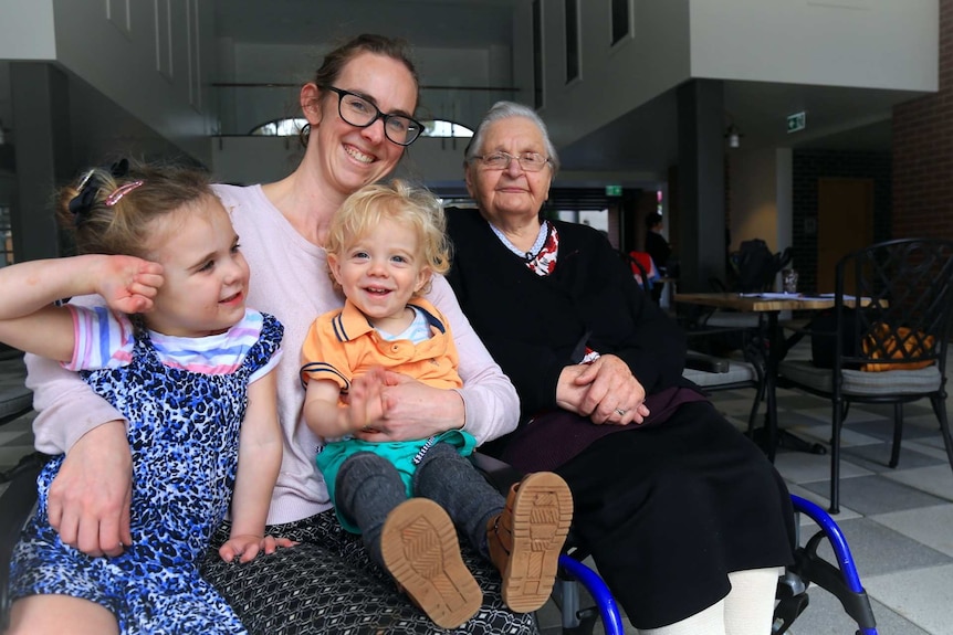 A mother and her young side smile at the camera alongside her daughter and an elderly resident.