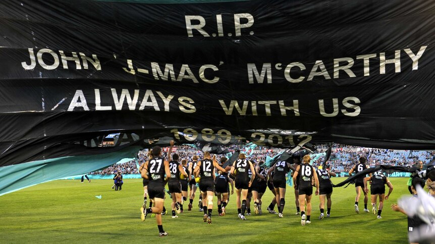 Fitting tribute ... Port Adelaide's players run through the banner during the memorial service for John McCarthy.