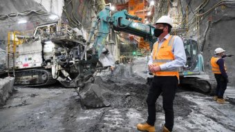 Daniel Andrews, dressed in a hard hat and high-vis, stands in front of heavy machinery on a construction site.