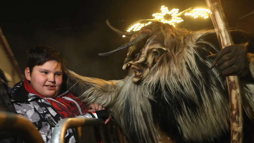 A participant dressed as the Krampus creature in search of delinquent children approaches a little boy.