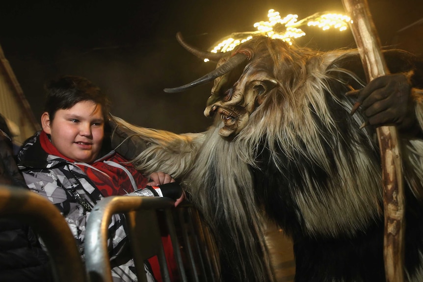 A participant dressed as the Krampus creature in search of delinquent children approaches a little boy.