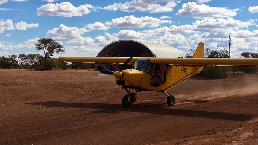 Small, yellow plane on dirt runway with hanger in background