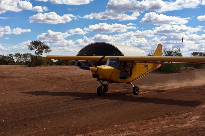 Small, yellow plane on dirt runway with hanger in background