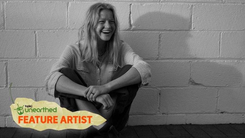 Lemon Myrtle, a young woman with blond hair and a button up shirt, sitting on the ground