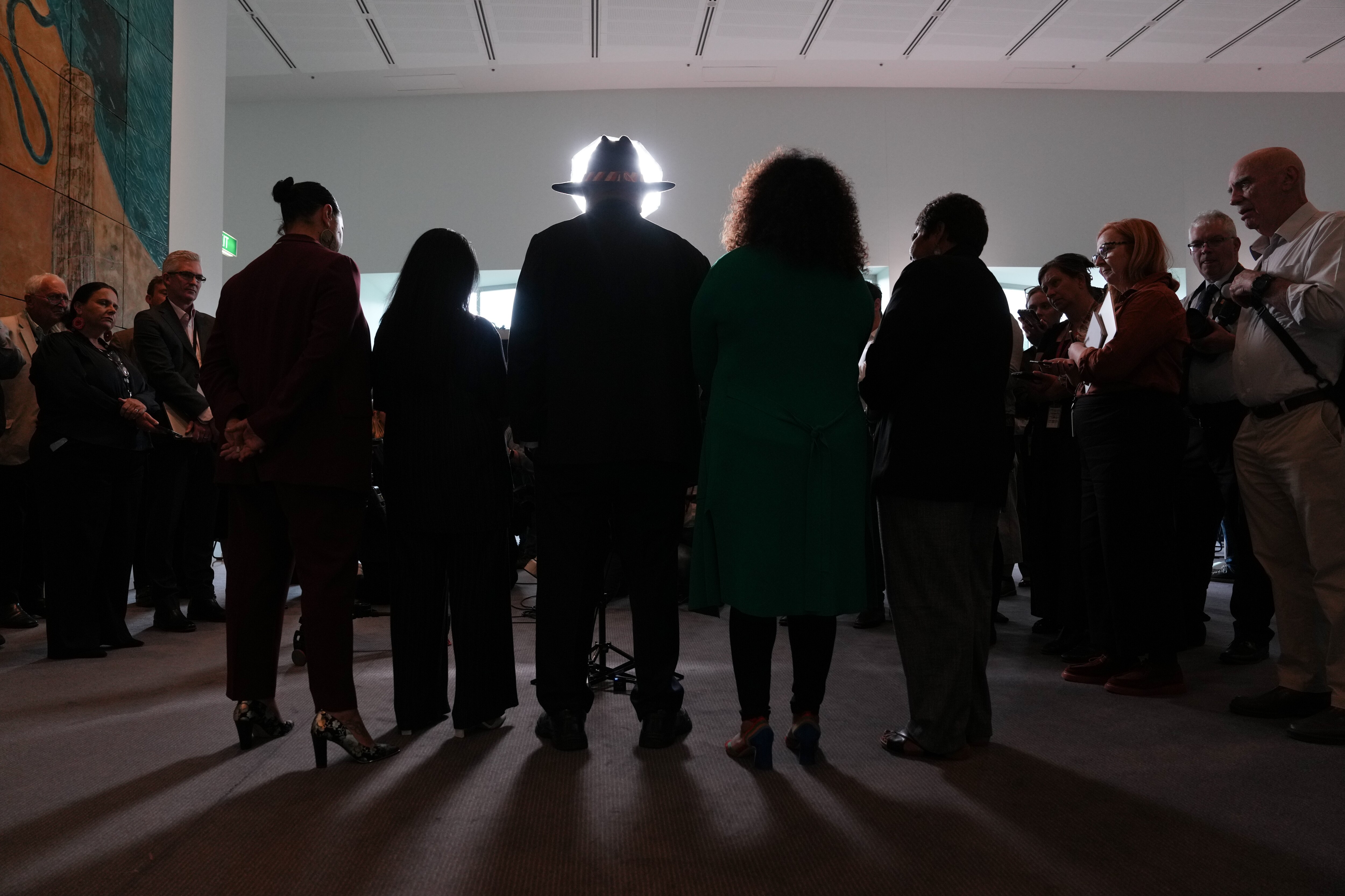 The silhouette of a group of people from behind. A wide-brimmed hat is visible in a circle of light.
