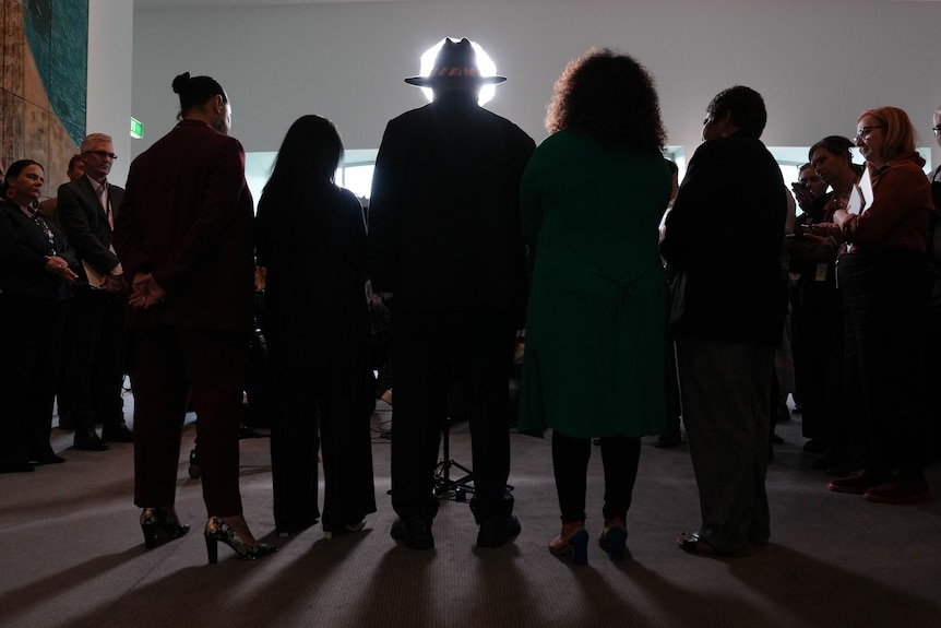 The silhouette of a group of people from behind. A wide-brimmed hat is visible in a circle of light.