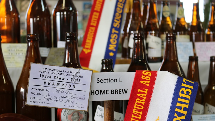 Brown bottles of beer lined up on pavilion stand with a champion red, white and blue ribbon on the winning beer.