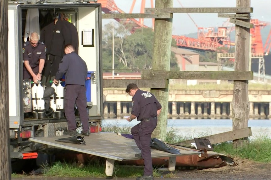 Police officer unload oxygen tanks and scuba diving gear on the side of a wharf.
