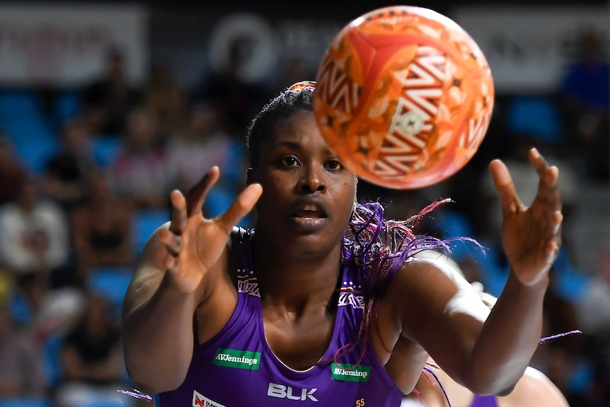 A Queensland Firebirds Super Netball player reaches out to catch the ball with both hands.
