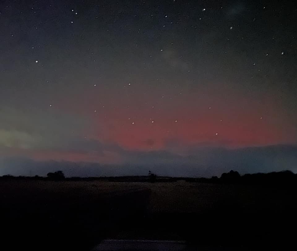 A dark paddock and sky with a red glow behind clouds. 